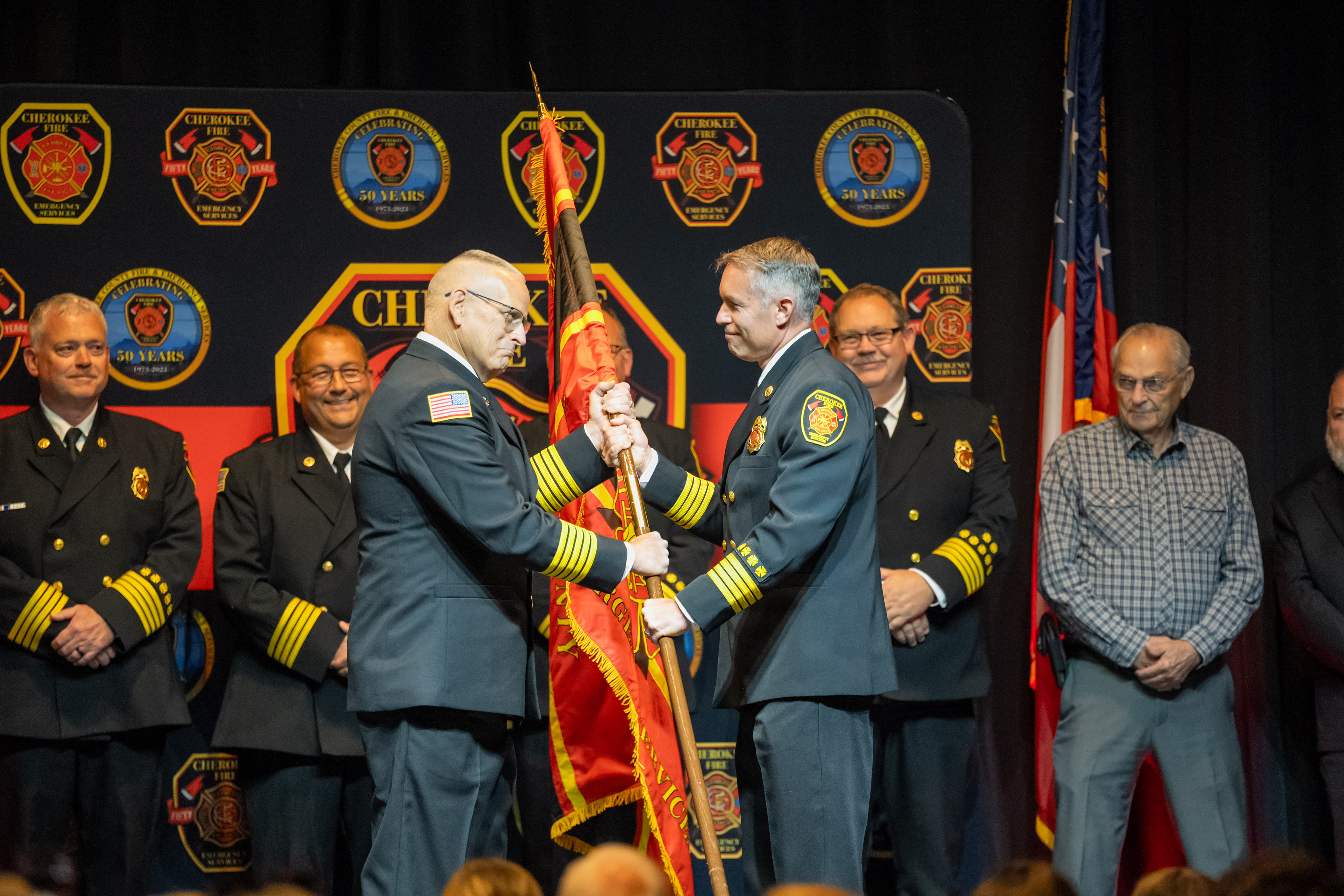 Outgoing Fire Chief Eddie Robinson passes the department colors to incoming Fire Chief Kevin Lanier.
